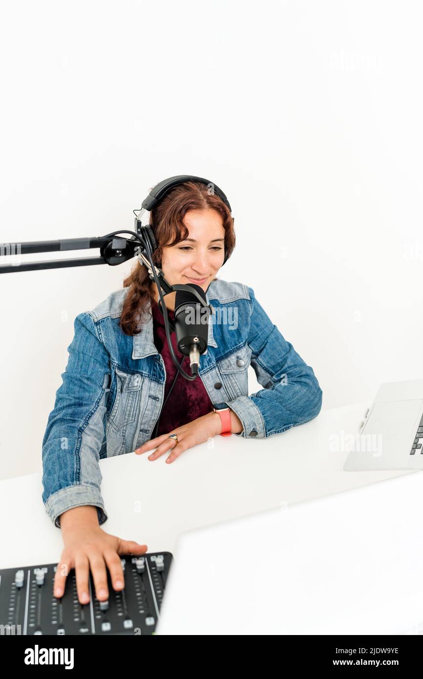 Frau, die vor dem Mikrofon lächelt und Kopfhörer mit der Hand auf dem Mischpult trägt Stockfoto