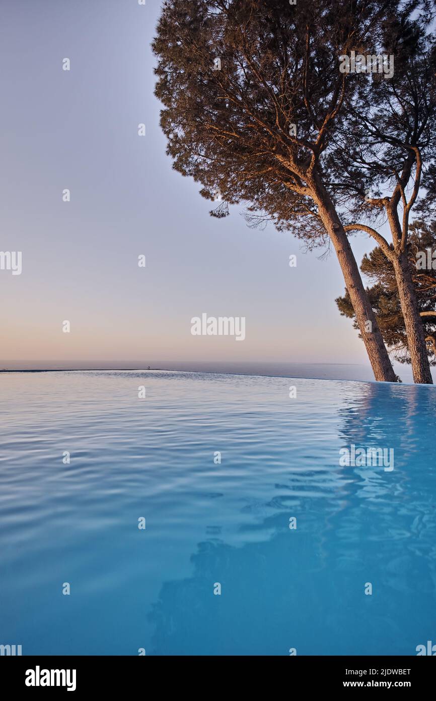 Ein unendlicher Pool mit Bäumen vor blauem Himmel mit Copyspace. Schöner Außenpool in einem Resort oder einer luxuriösen Ferienvilla Stockfoto
