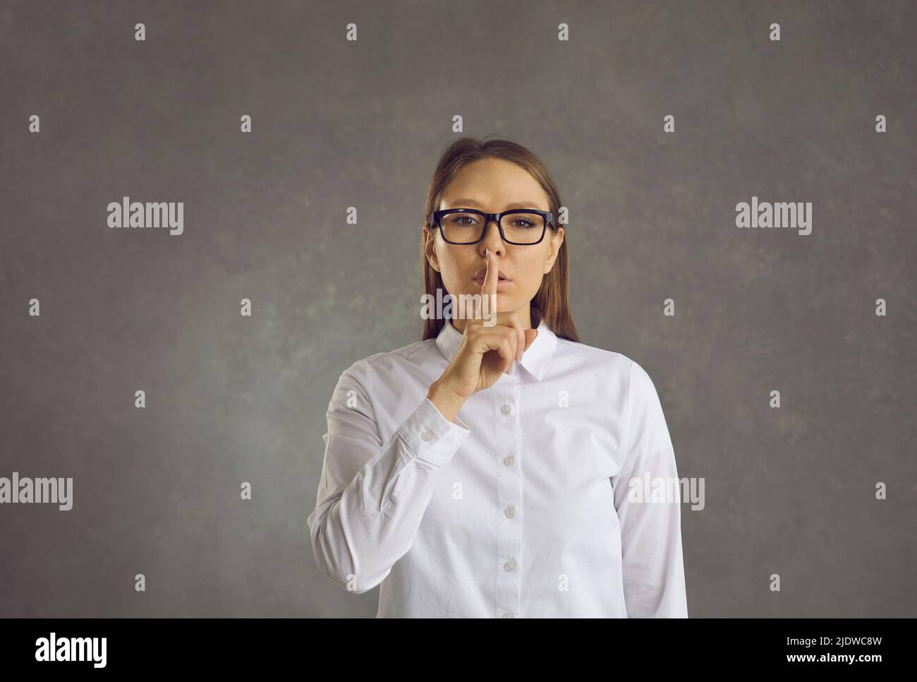 Seriöse Frau bittet um Ruhe, indem sie ihren Zeigefinger auf ihre Lippen drückt und sie scheut. Stockfoto