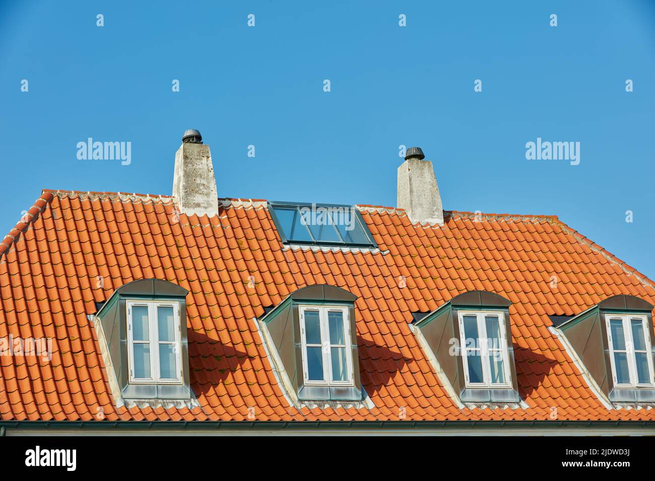 Schornsteine, Fenster und Dachfenster, die auf dem Hausgebäude draußen vor blauem Himmel gestaltet wurden. Bau der Außenarchitektur auf Stockfoto