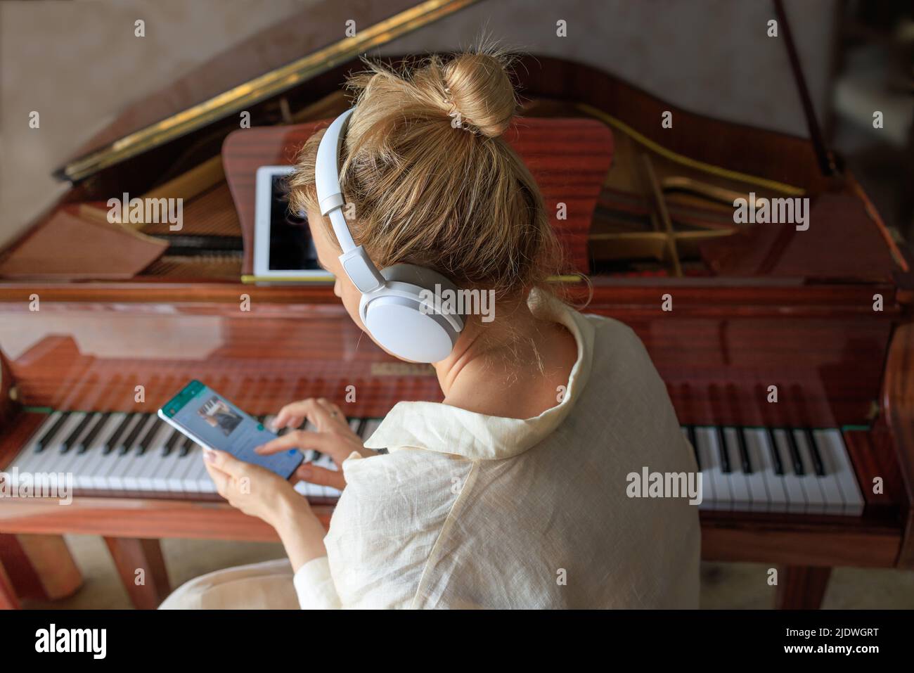 Ein junges Mädchen mit Kopfhörern spielt ein antikes Klavier und nutzt ein Smartphone zum Lernen Stockfoto