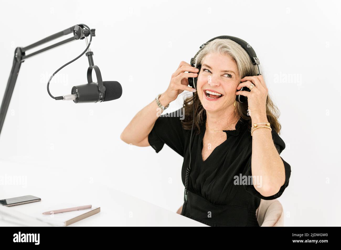 Frau mit Kopfhörern, die vor dem Mikrofon sitzt und lacht Stockfoto