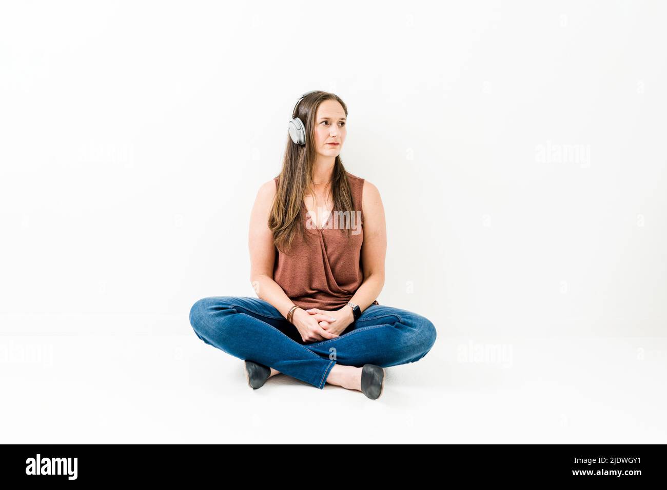Frau, die auf dem Boden sitzt und Kopfhörer hört, die in der Ferne abblicken Stockfoto