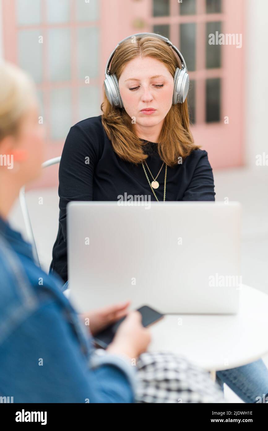 Zwei Frauen, die an einem Telefon und einem Laptop mit Kopfhörern in der Nähe einer pinken Tür arbeiten Stockfoto