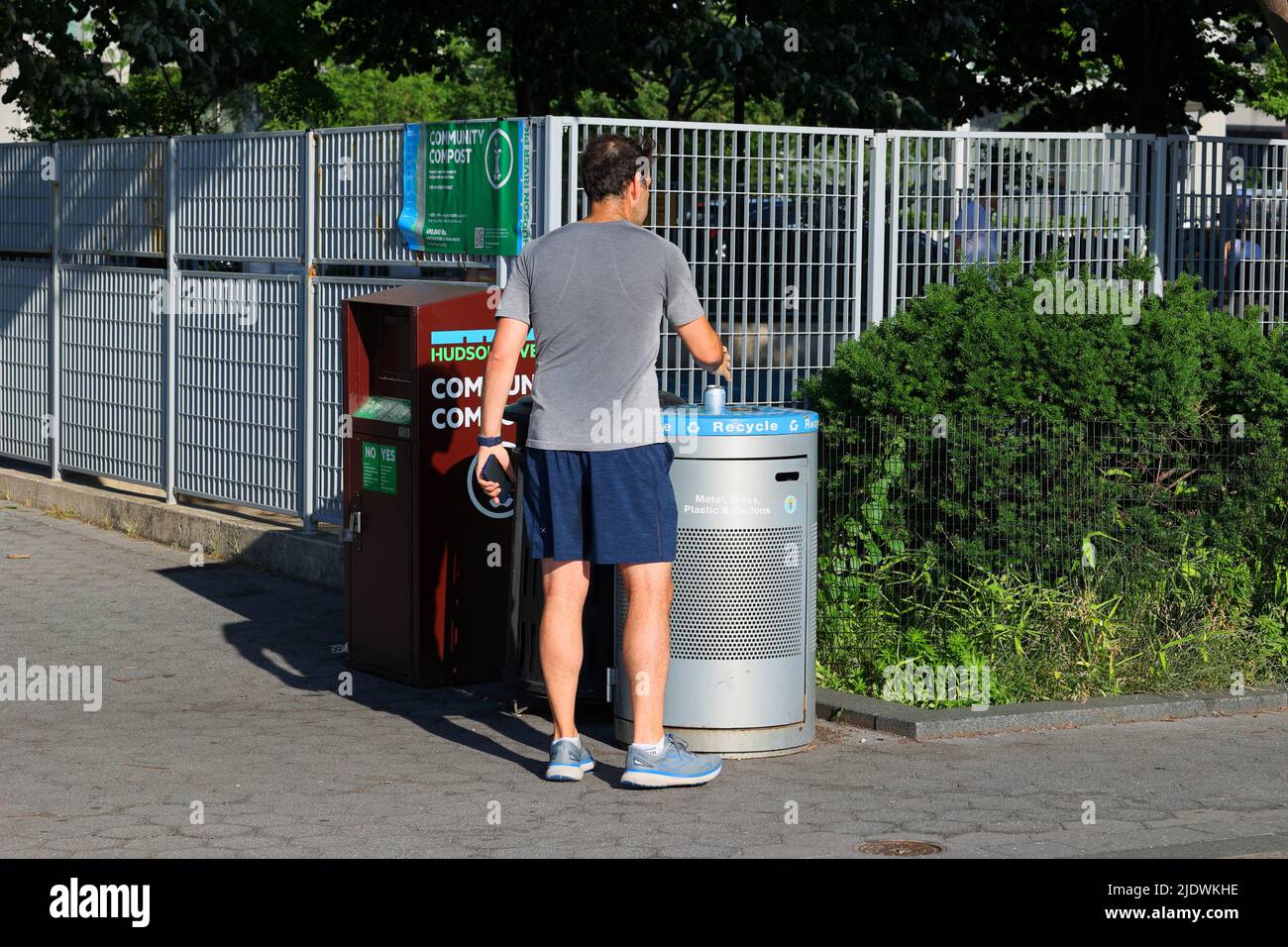 Eine Person wirft einen recycelbaren Gegenstand in einen NYC-Recyclingbehälter im Hudson River Park. Eine Person, die in New York City recycelt. Stockfoto