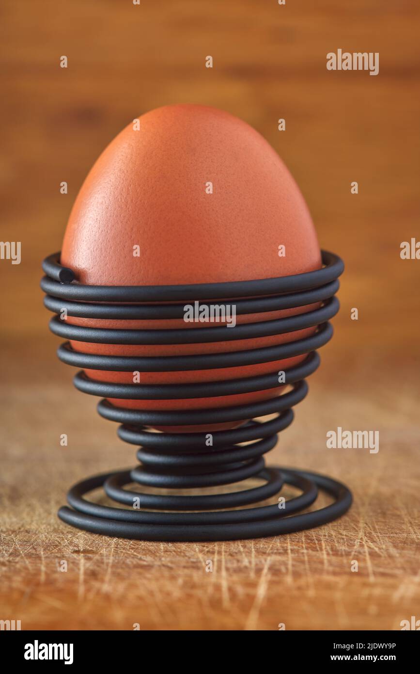 Ein gekochtes Ei in einer spiralförmigen Metallstütze auf Holzhintergrund Stockfoto