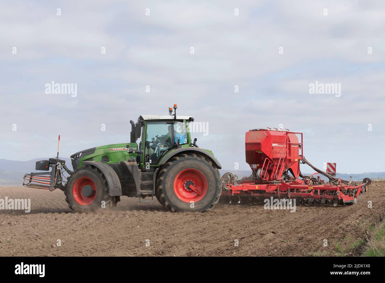 Ein Fendt-Traktor, der einen roten Bohrer zieht und sich am Ende des Feldes dreht, in dem er sät Stockfoto