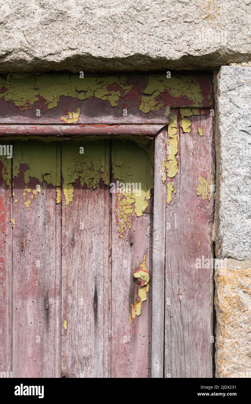 Die obere Ecke einer alten, kalkgrünen Holztür, umrahmt von Granitblöcken, mit Peeling-Gemälde mit verblassten kastanienbraunen Farben und Holzwürmern darunter Stockfoto