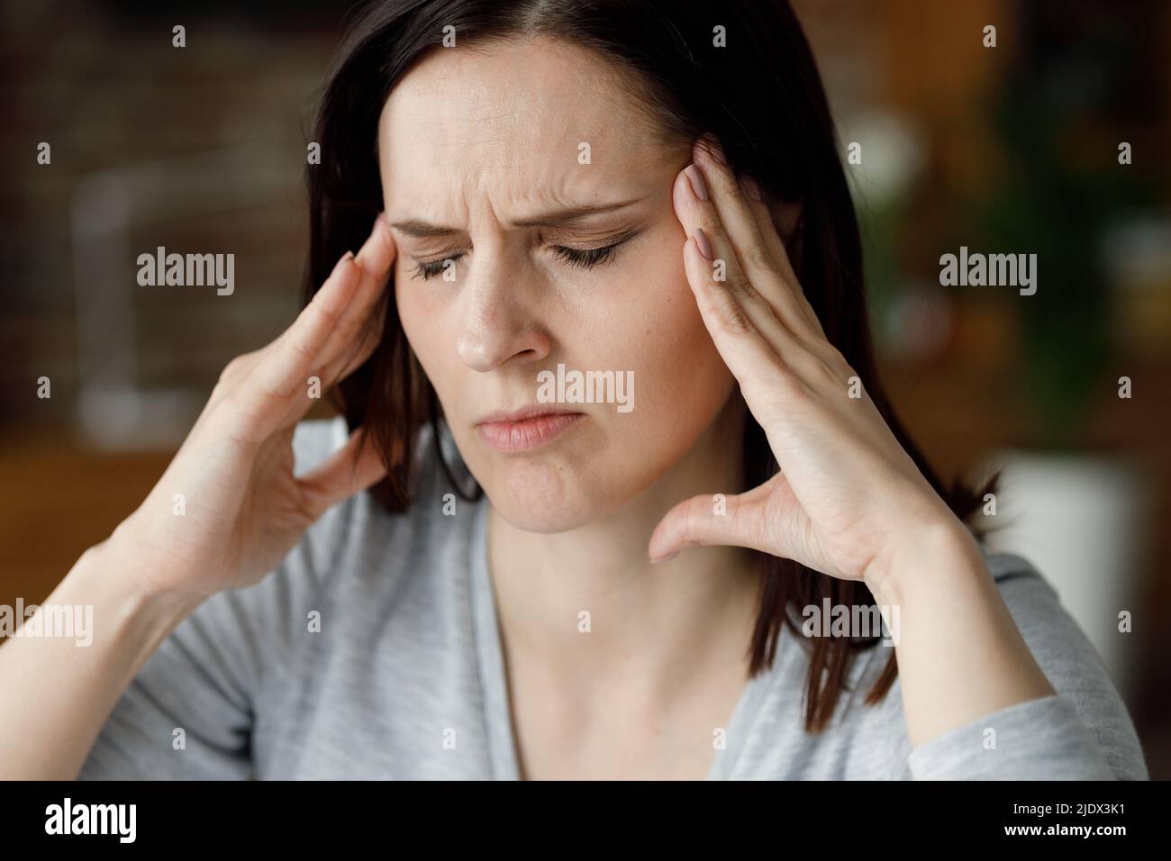 Verärgerte junge Frau, die unter Kopfschmerzen leidet. Erschöpfte Frau mit geschlossenen Augen massiert die Schläfen mit schmerzhaften Empfindungen. Migräne, hohes Blut Stockfoto