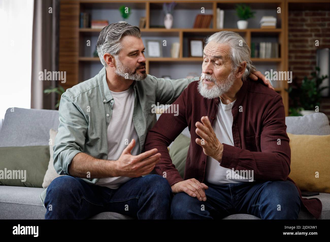 Ein älterer Vater beschwert sich über das Leben eines erwachsenen Sohnes, was ihm hilft, die Morgendämmerung zu beruhigen. Zwei Generationen Familie hat Gespräche, teilen Nachrichten, Ausgaben Stockfoto