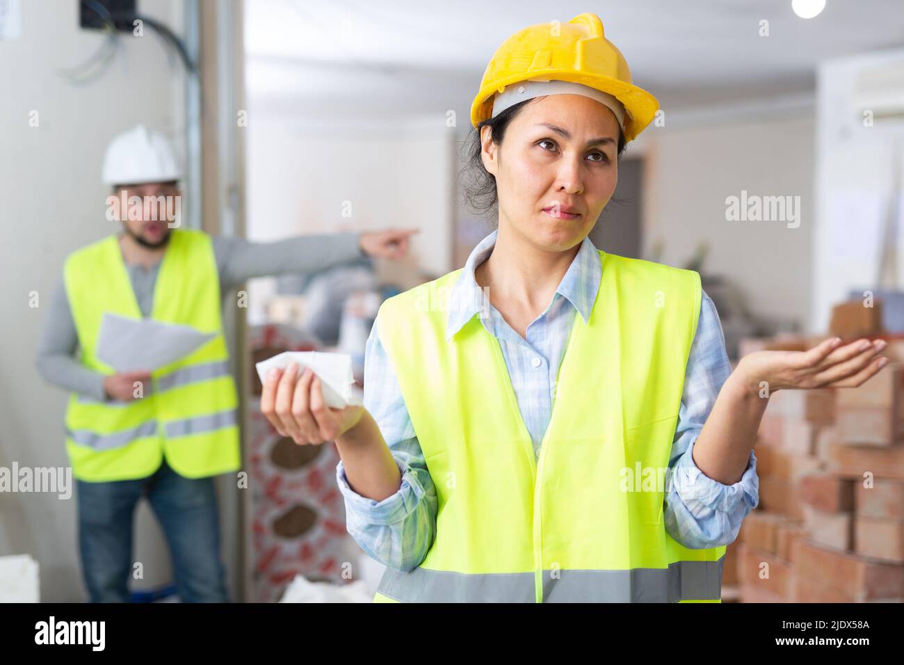 Verwirrte Ingenieurin und schreiender Vorarbeiter auf der Baustelle Stockfoto