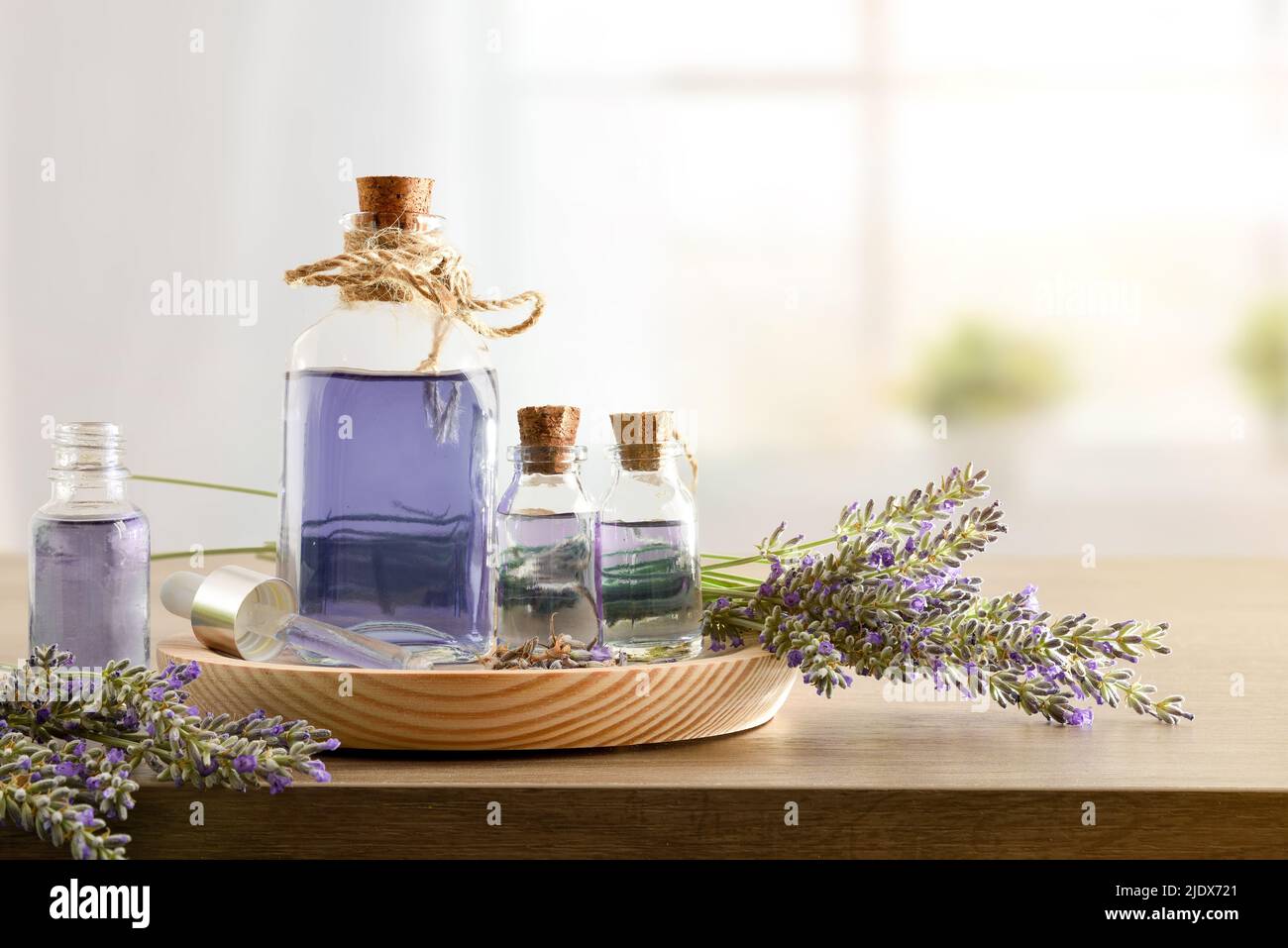 Glasbehälter mit Lavendelessenz mit Blumensträußen von Stacheln auf Holz in einem Raum. Vorderansicht. Horizontale Zusammensetzung. Stockfoto