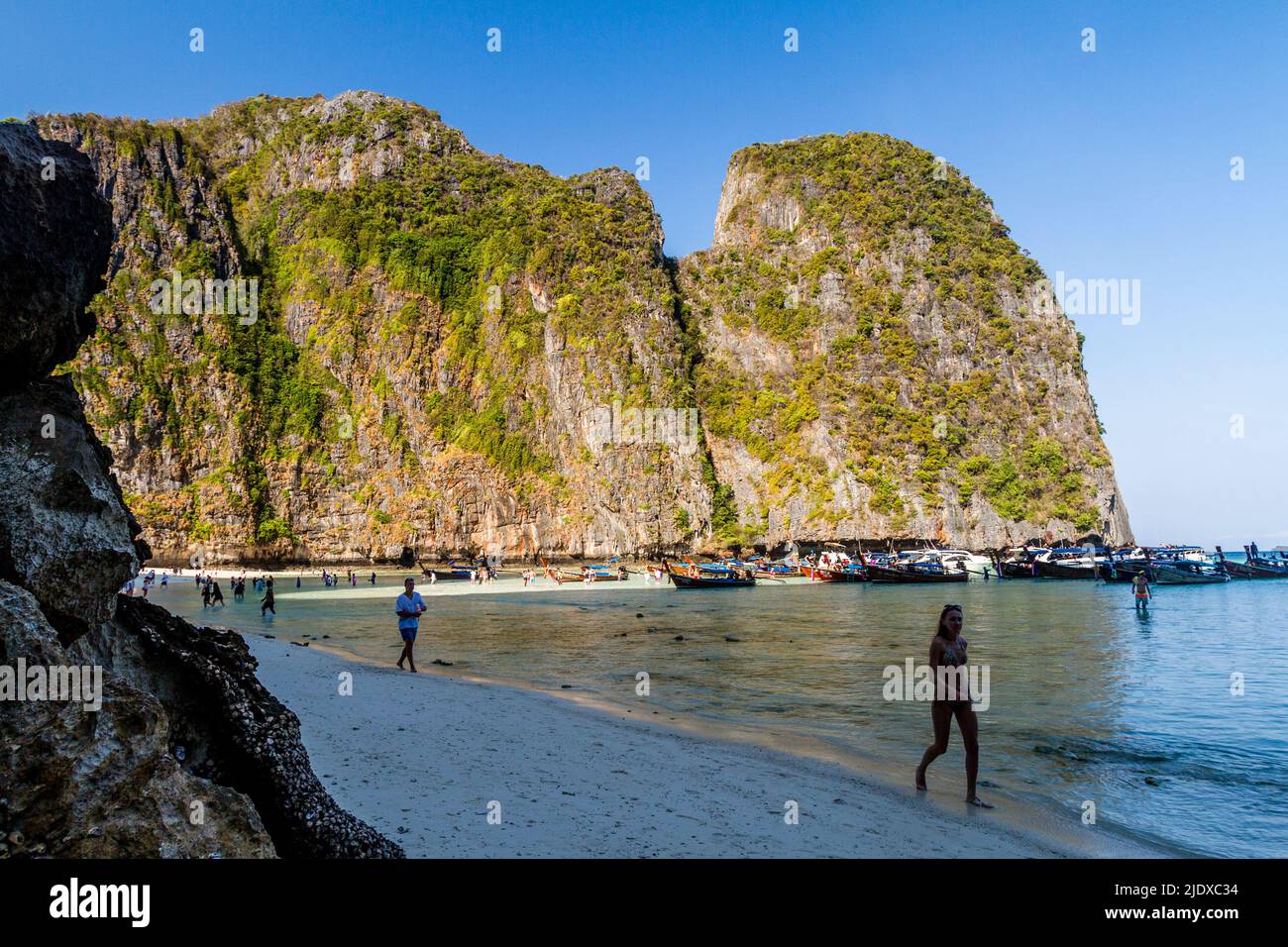 Eine wunderschöne Bucht mit großen Kalksteinfelsen und Menschen, die im Schatten am Strand spazieren. Stockfoto