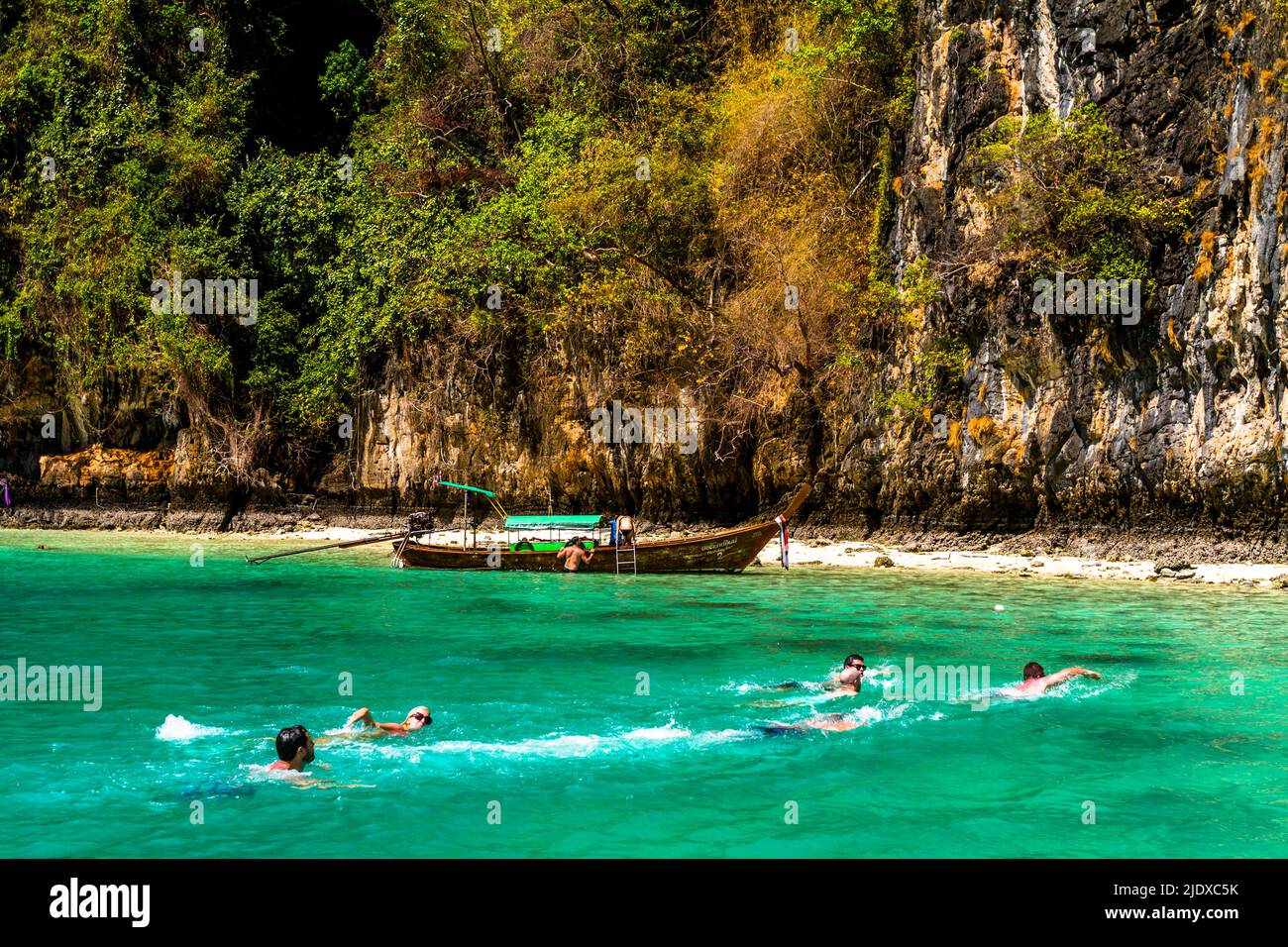 Schwimmer im türkisfarbenen Wasser der thailändischen Phi Phi Inseln. Der Strand und ein großer Felsen sehen aus wie ein Paradies. Stockfoto