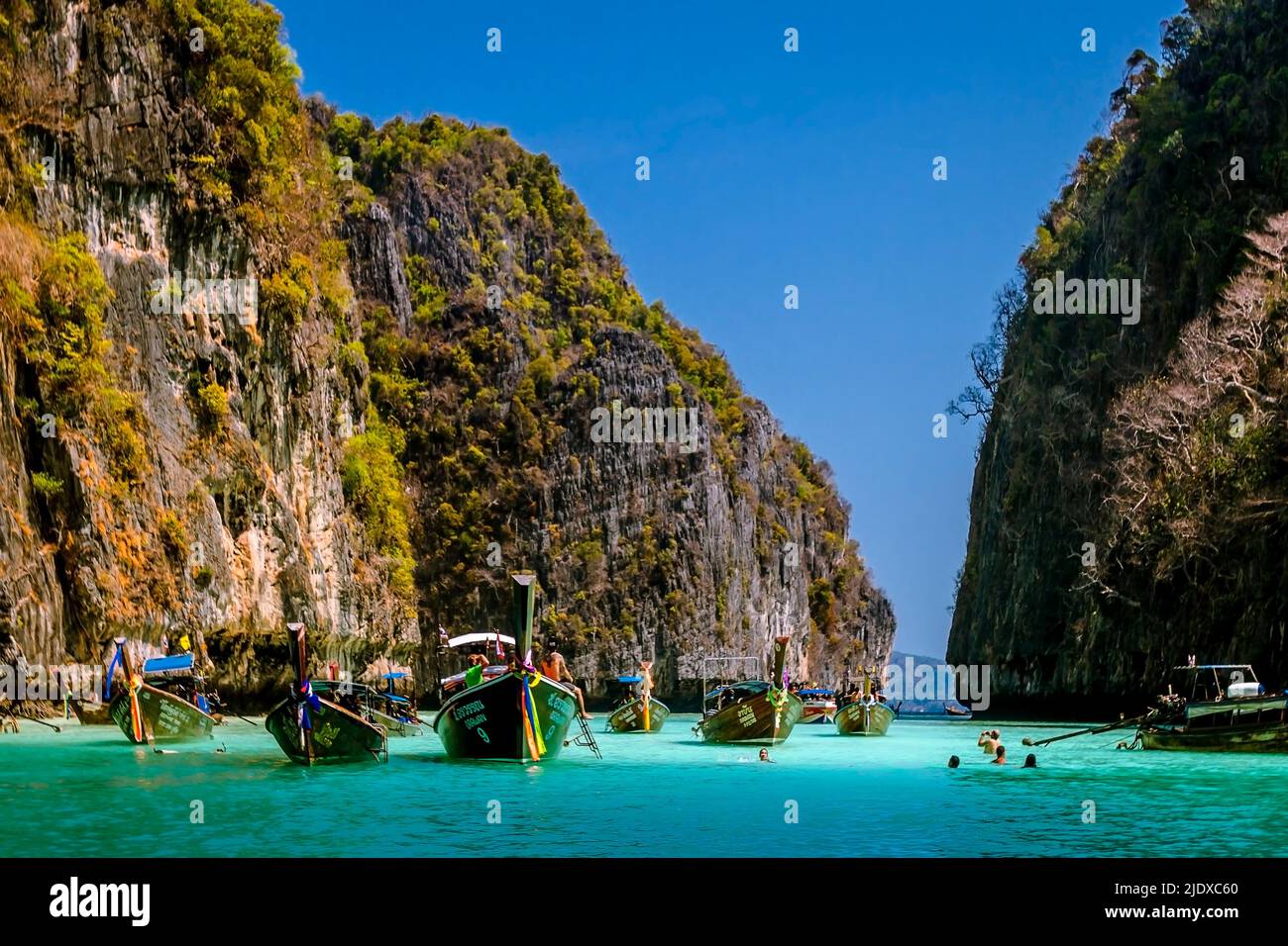 Phi Phi Inseln Zwischen zwei Kalksteinfelsen ist eine Bucht mit vielen Langschwanz-Touristenbooten, die in blauem seichtem Wasser verankert sind. Stockfoto