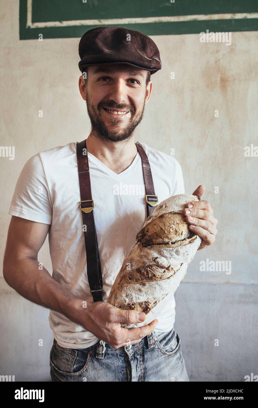 Lächelnder Bäckerbesitzer, der frisch gebackenes Landbrot hält Stockfoto