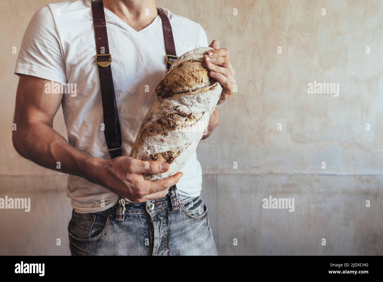 Bäcker hält frisch gebackenes Landbrot vor der Wand in der Bäckerei Stockfoto