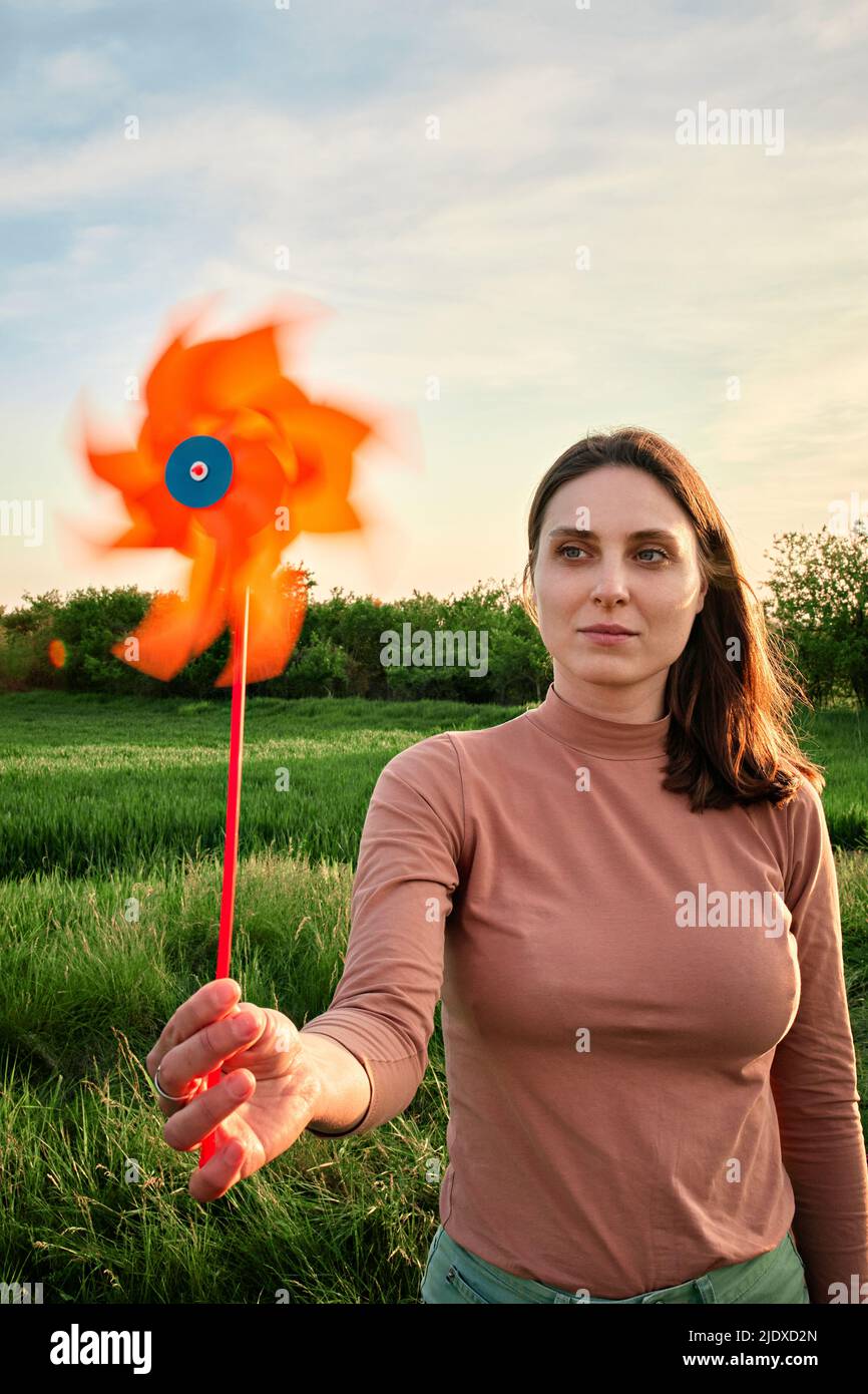 Junge Frau hält bei Sonnenuntergang ein Windrad-Spielzeug auf dem Feld Stockfoto