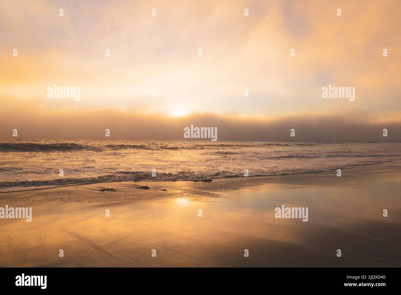 Sonnenuntergang am Strand mit Meereswolken, die zum Ufer hin Rollen Stockfoto