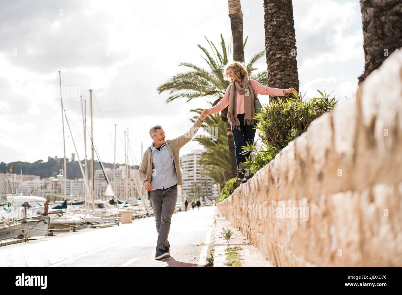Reifer Mann, der die Hand einer Frau hält, die im Urlaub an der Wand läuft Stockfoto