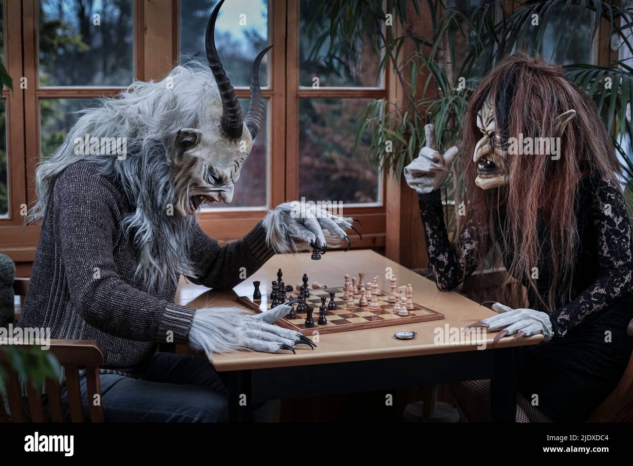 Reifer Mann und Frau im Geisterkostüm spielen Schachspiel am Tisch sitzend Stockfoto