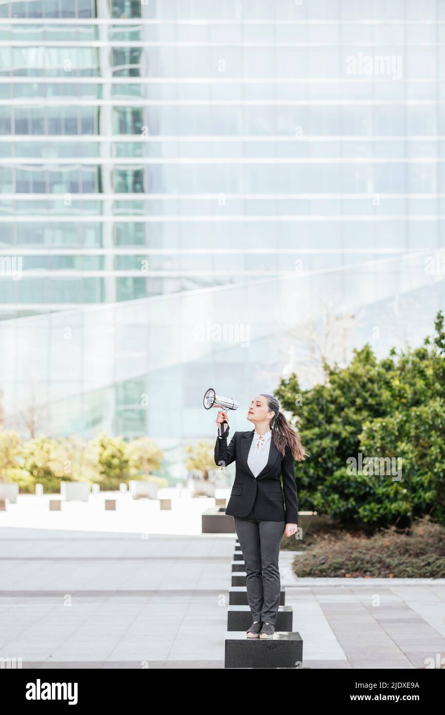 Geschäftsfrau, die vor dem Bürogebäude durch das Megaphon spricht Stockfoto