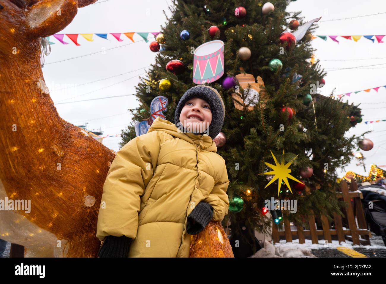 Junge mit Strickmütze steht bei Hirsch Dekoration auf dem Weihnachtsmarkt Stockfoto