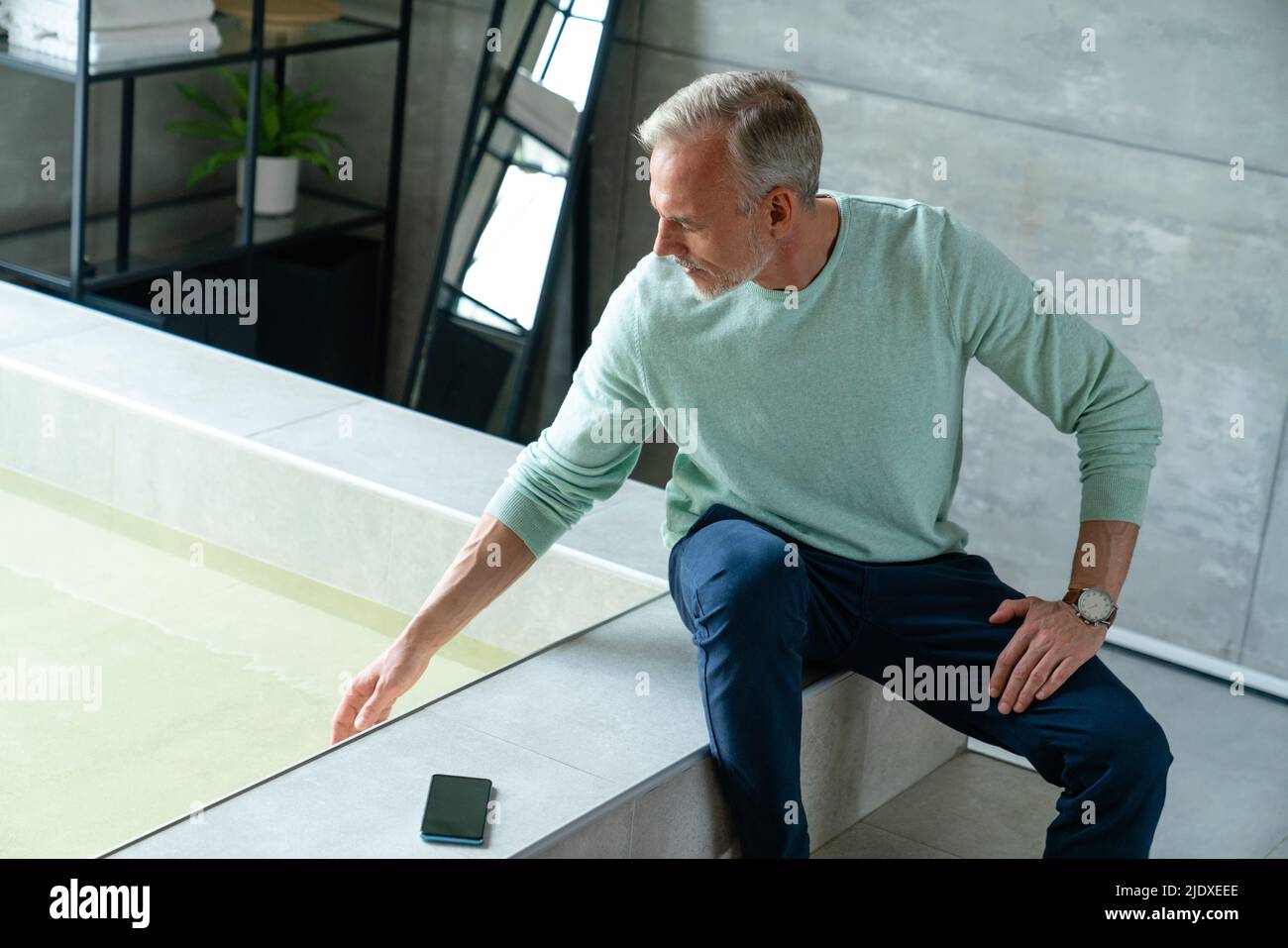 Mann, der zu Hause in der Badewanne Wasser anfasst Stockfoto