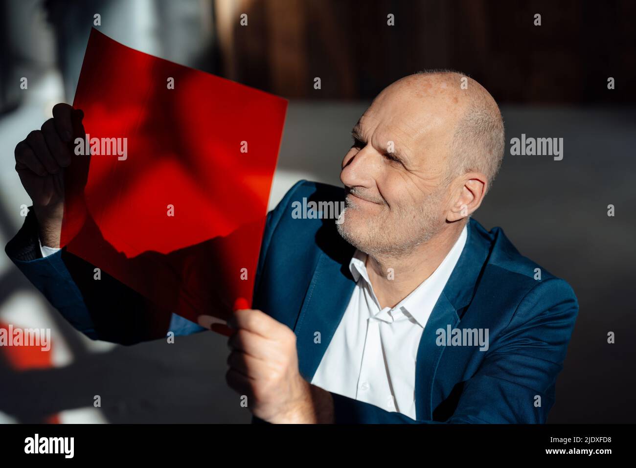 Lächelnder Geschäftsmann, der rote Zellophane im Büro ansieht Stockfoto