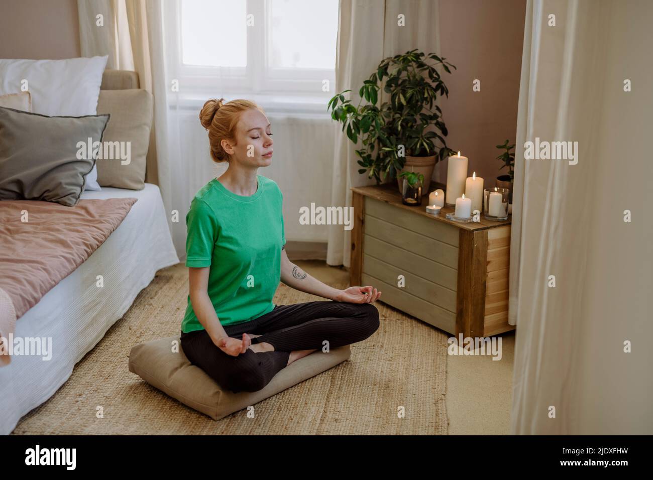 Frau, die zu Hause mit gekreuzten Beinen sitzt und Atemübungen praktiziert Stockfoto