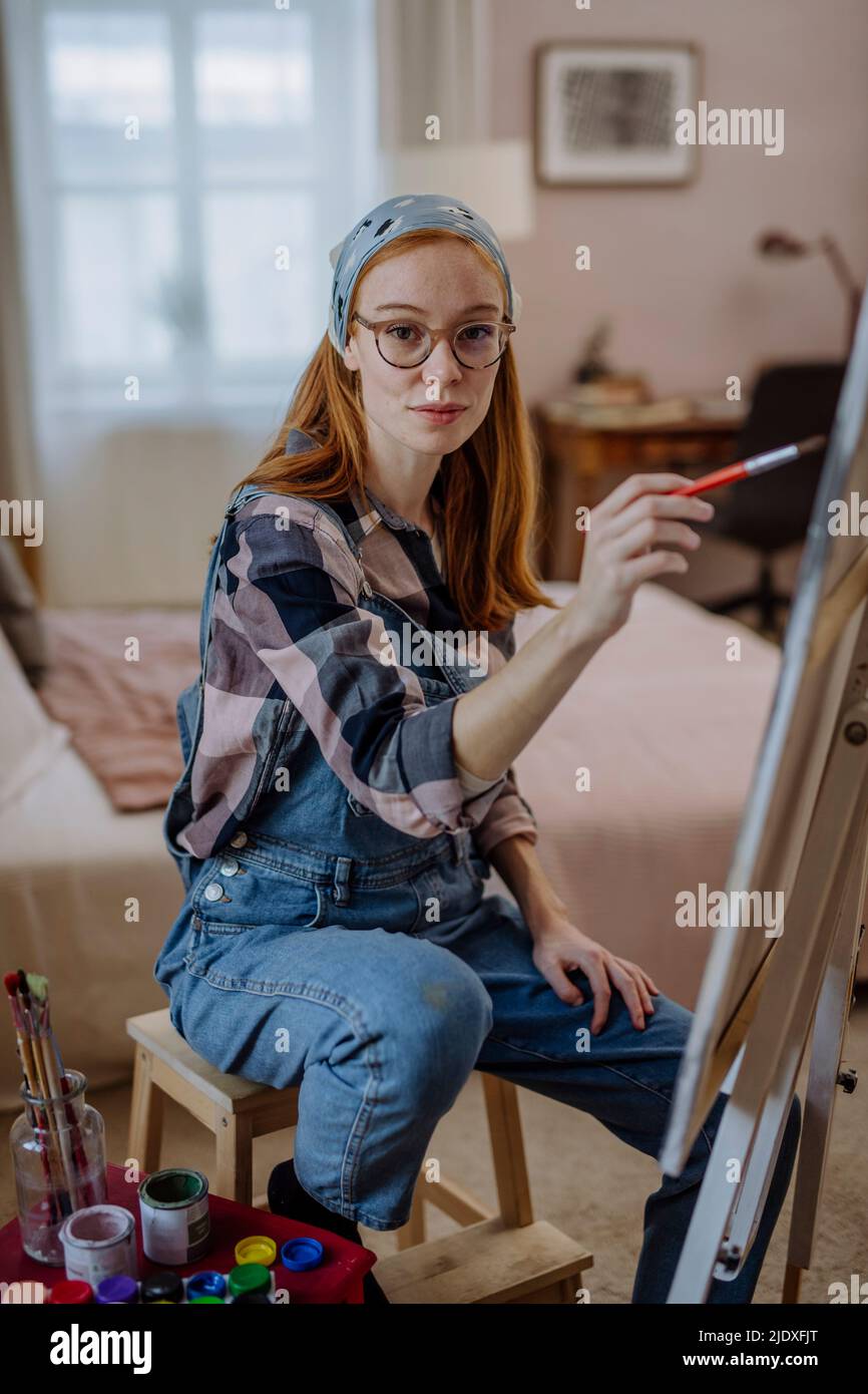 Frau mit Brille sitzt zu Hause auf dem Hocker auf der Leinwand des Künstlers Stockfoto
