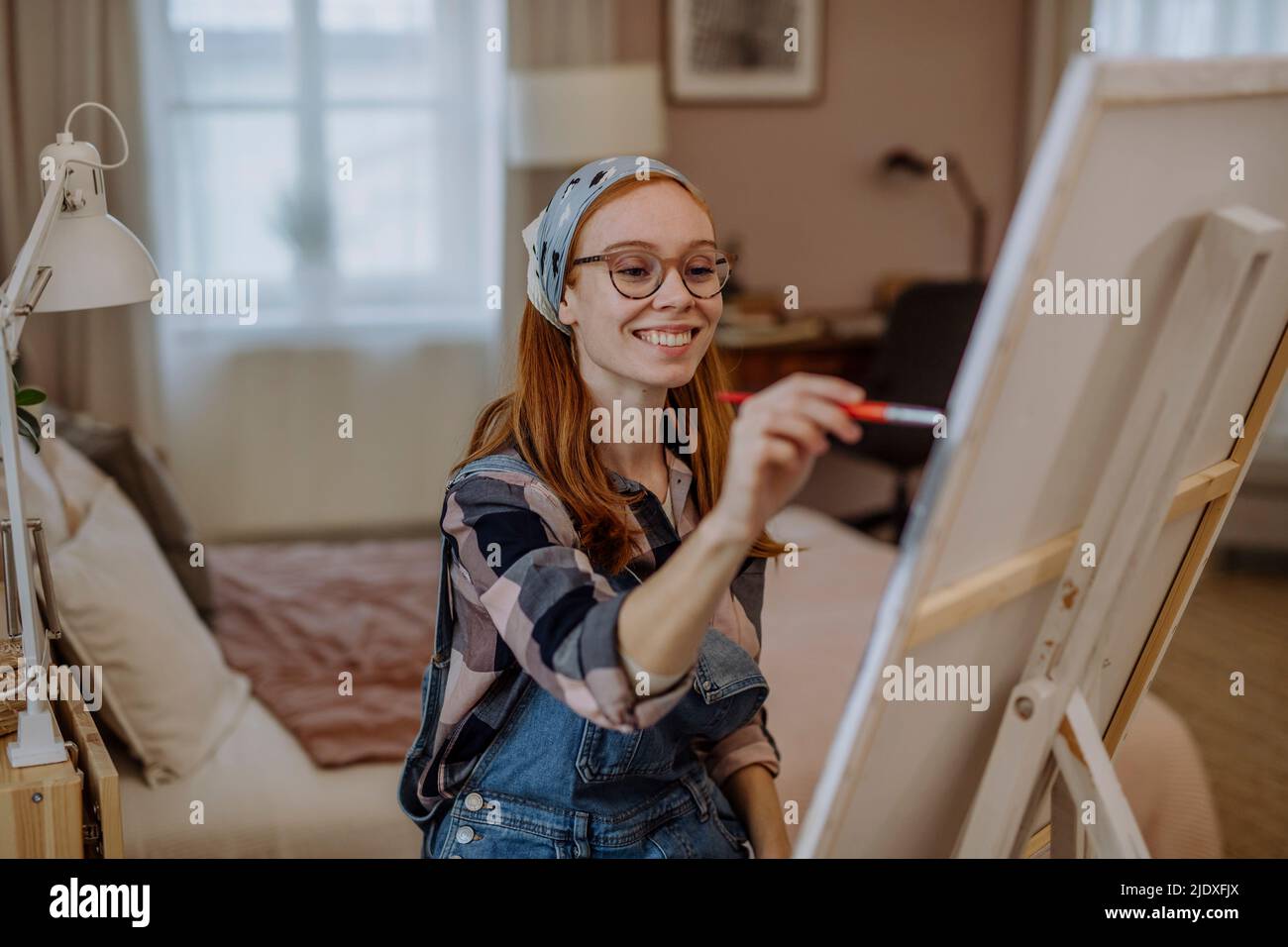 Glückliche Frau, die zu Hause Bandana auf der Leinwand des Künstlers trägt Stockfoto