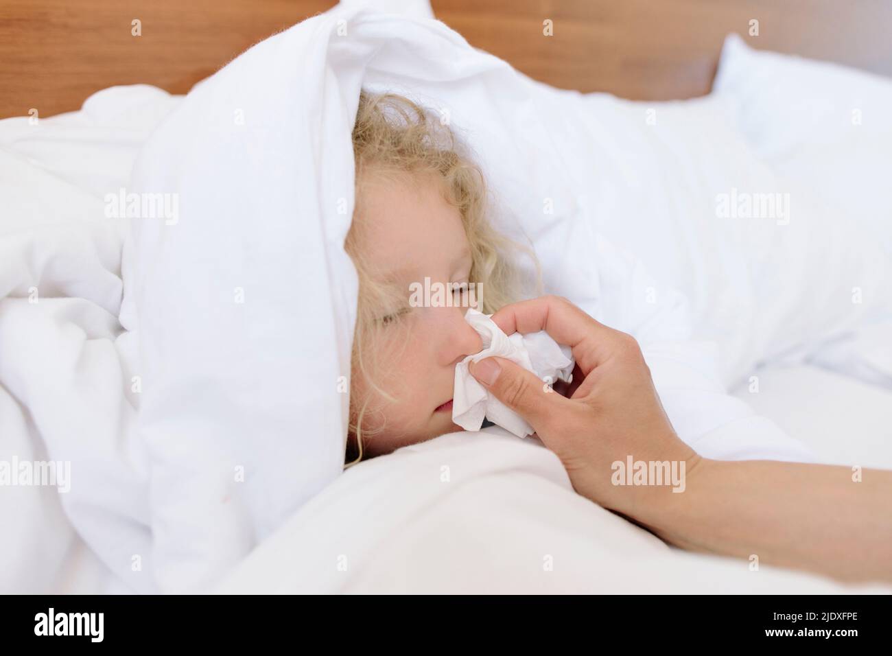 Mutter wischte die Nase der Tochter, die zu Hause auf dem Bett lag Stockfoto