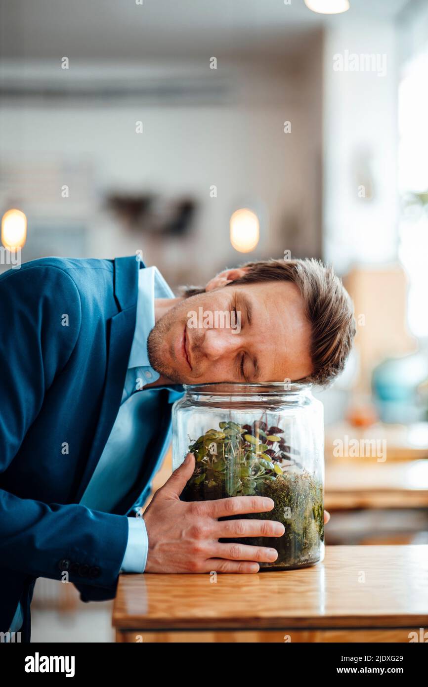 Reifer Geschäftsmann, der sich im Café auf einen Glasbehälter mit Pflanze stützt Stockfoto