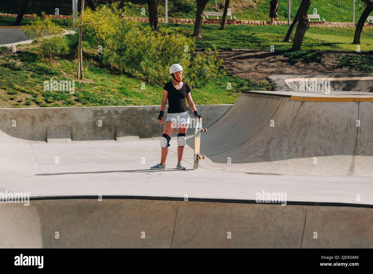 Frau trägt schützende Sportkleidung und hält Skateboard auf der Rampe Stockfoto