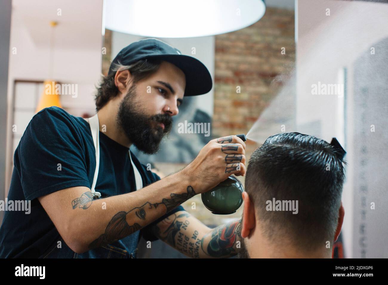 Friseur sprüht Wasser auf die Haare des Kunden im Friseurladen Stockfoto