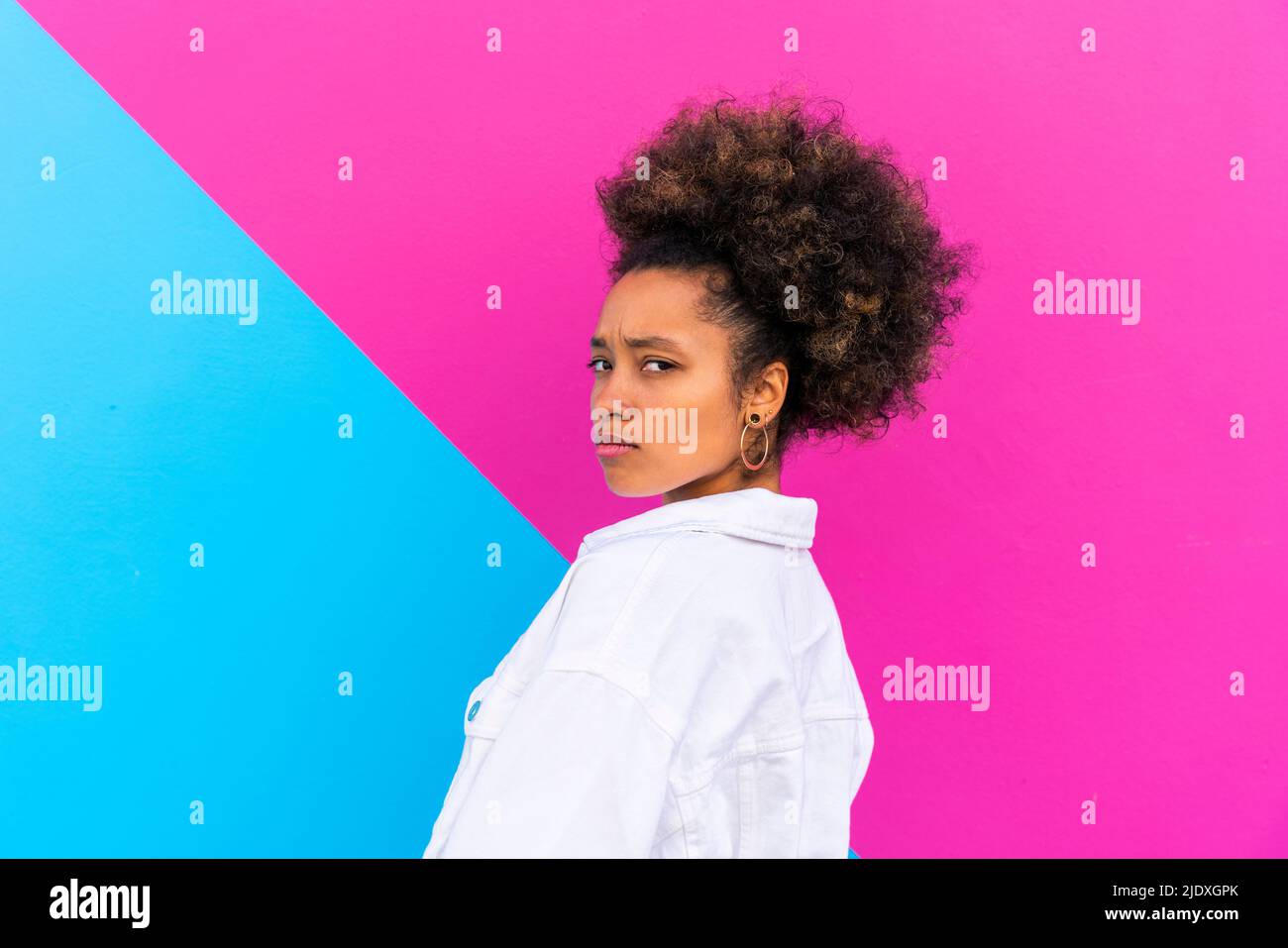 Frau mit Afro-Frisur vor rosa und blauer Wand runzeln Stockfoto