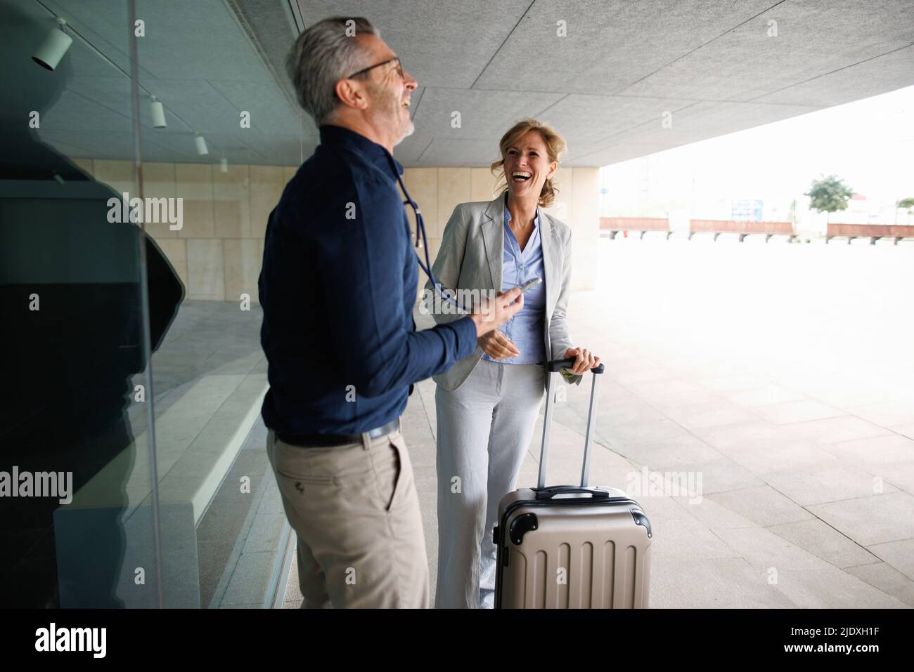 Fröhliche Geschäftsfrau und Geschäftsfrau mit Koffer an der Glaswand Stockfoto