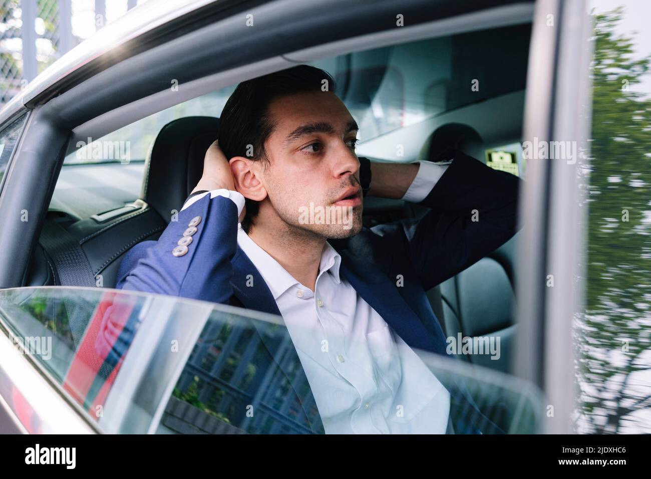 Geschäftsmann mit der Hand in den Haaren sitzt auf dem Rücksitz in einem Elektroauto Stockfoto