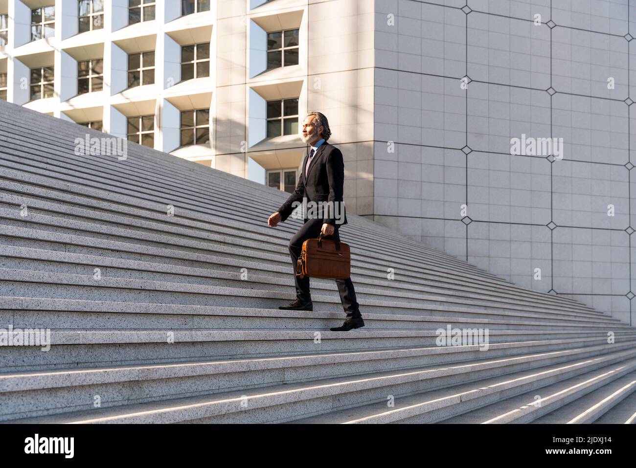 Reifer Geschäftsmann mit Tasche, die sich auf der Treppe nach oben bewegt Stockfoto