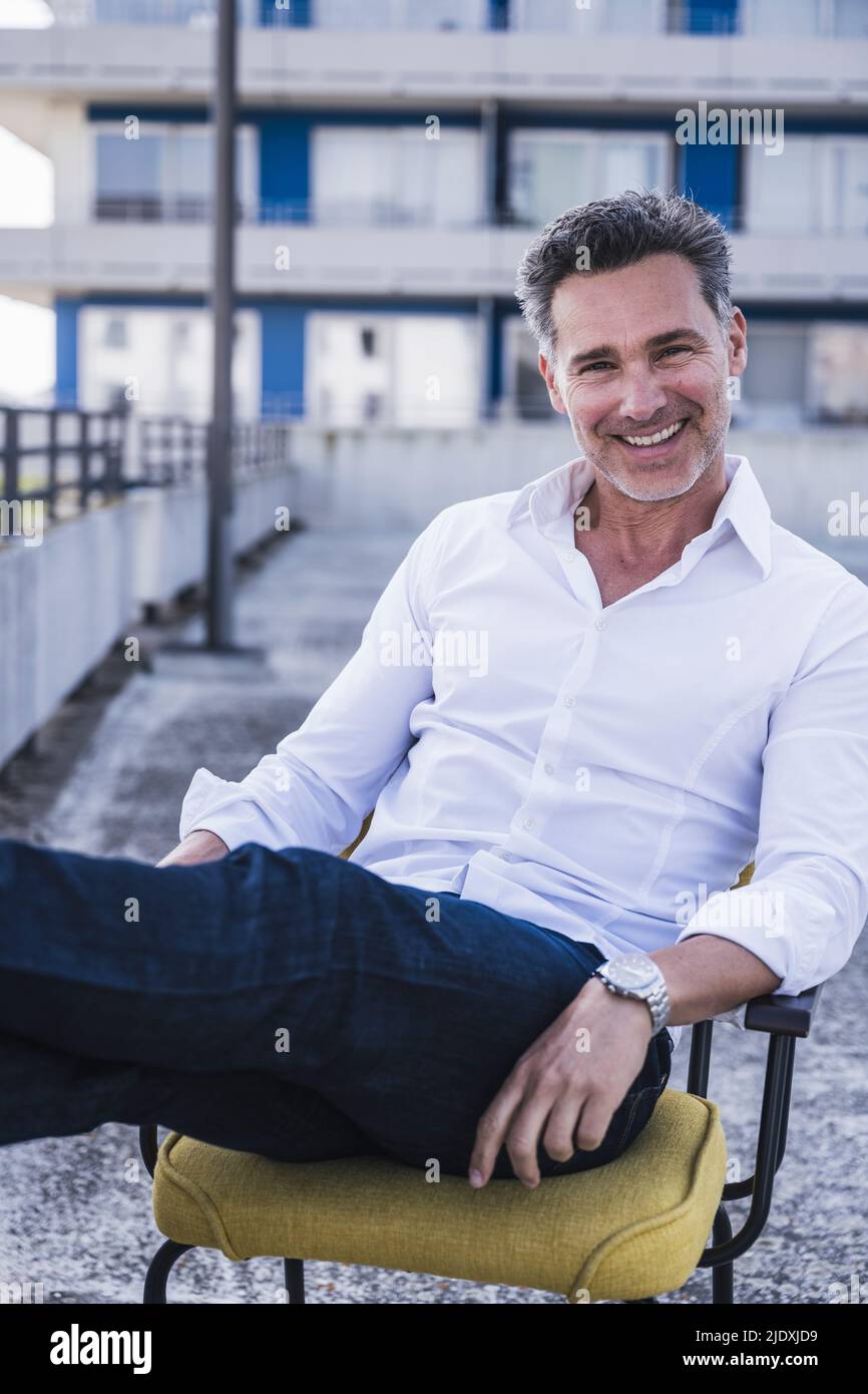 Fröhlicher, reifer Geschäftsmann, der auf einem Stuhl sitzt Stockfoto