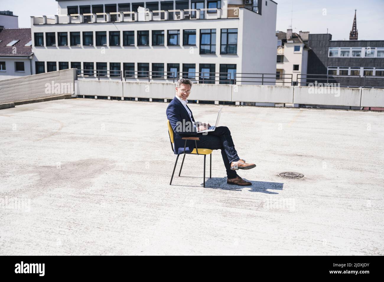 Lächelnder Geschäftsmann, der mit einem Laptop auf einem Stuhl sitzt Stockfoto