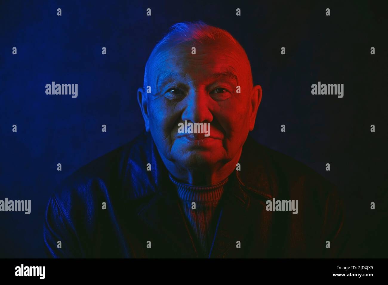 Das Gesicht des älteren Mannes wurde mit rotem und blauem Neonlicht vor schwarzem Hintergrund beleuchtet Stockfoto