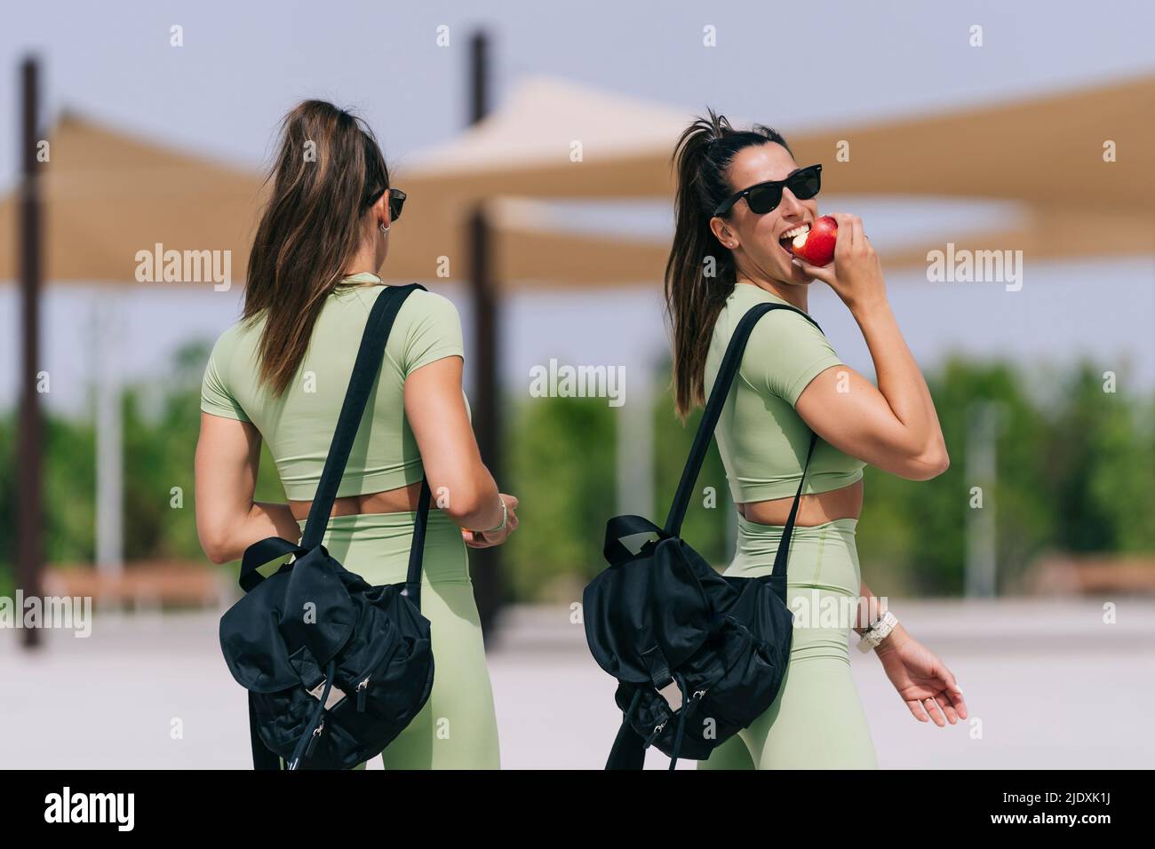 Frau im Rucksack, die an sonnigen Tagen durch die Zwillingsschwester beim Apfelessen geht Stockfoto