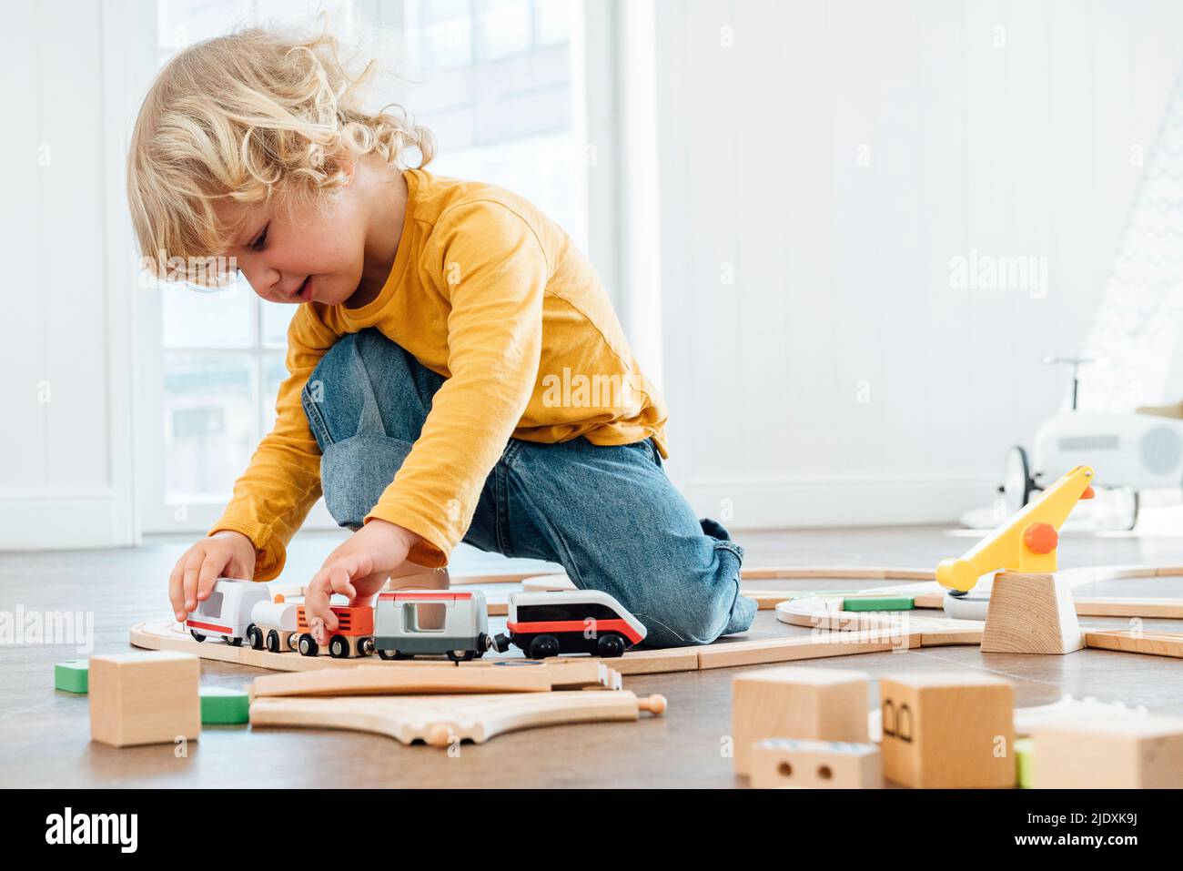 Niedlicher Junge mit blonden Haaren, der zu Hause mit dem Spielzeug-Zug spielt Stockfoto