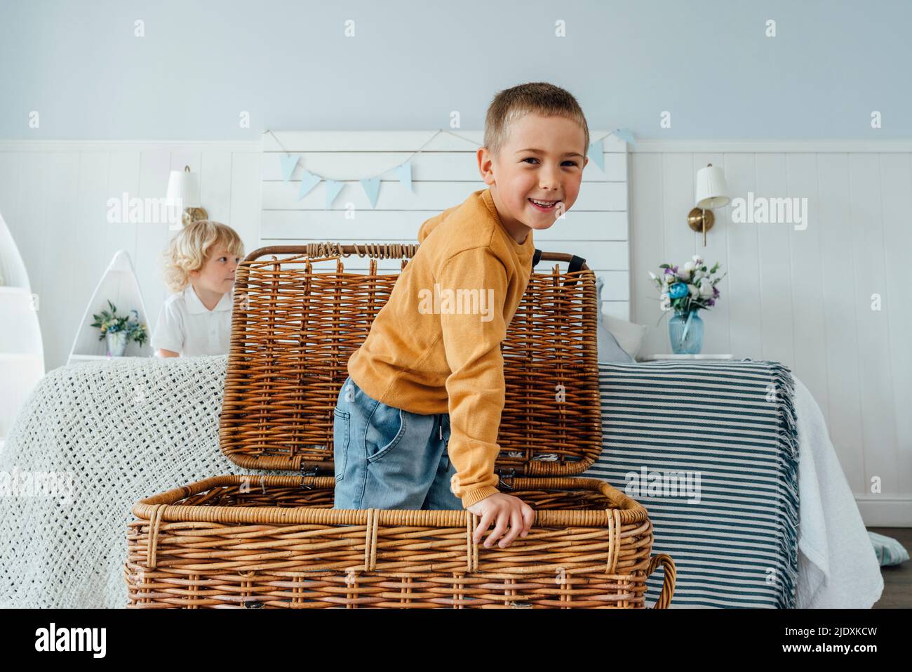 Fröhlicher Junge, der zu Hause im Korbkorb am Bett steht Stockfoto