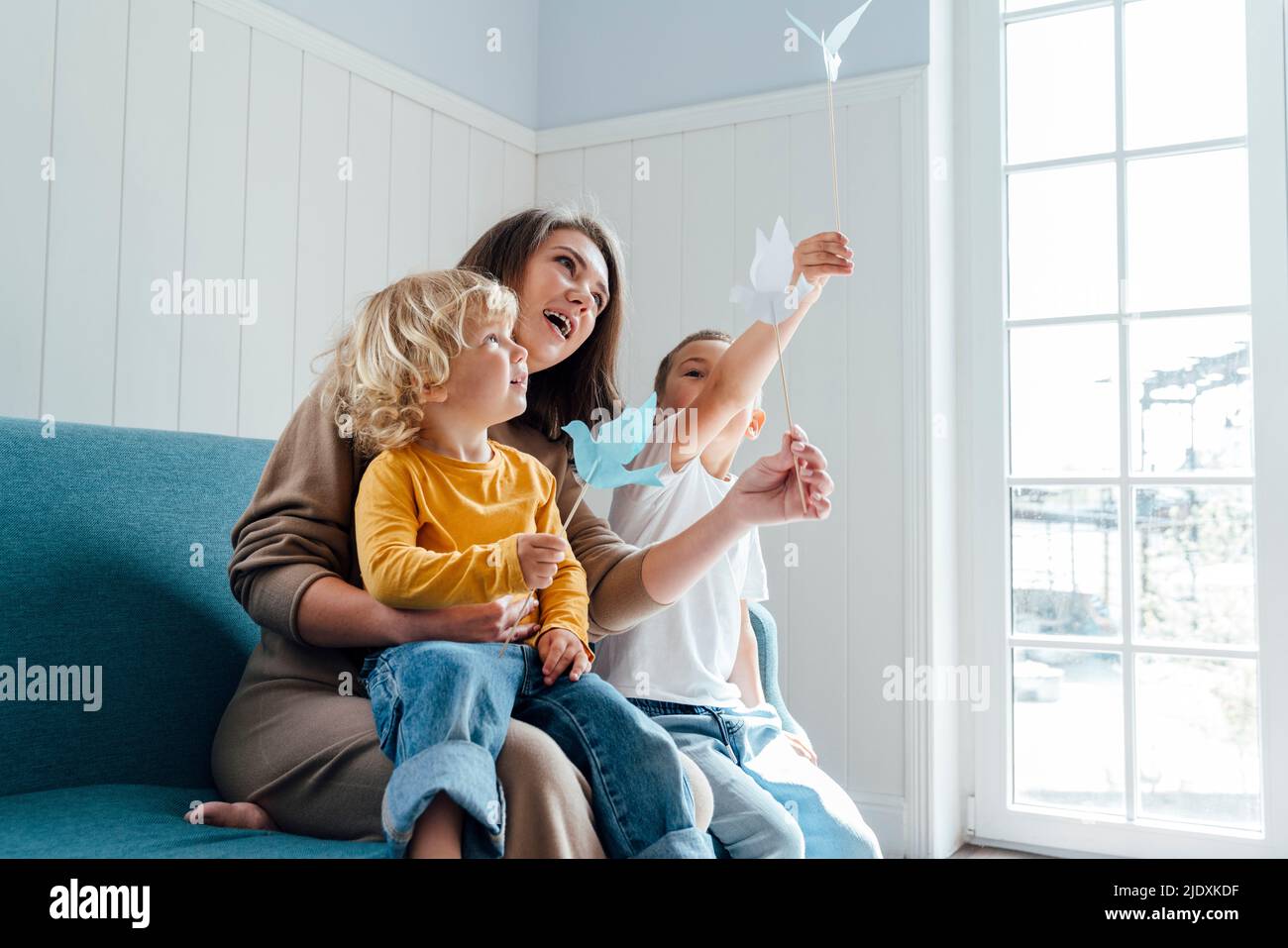 Mutter und Sohn spielen mit Origami-Vögeln, die zu Hause auf dem Sofa sitzen Stockfoto