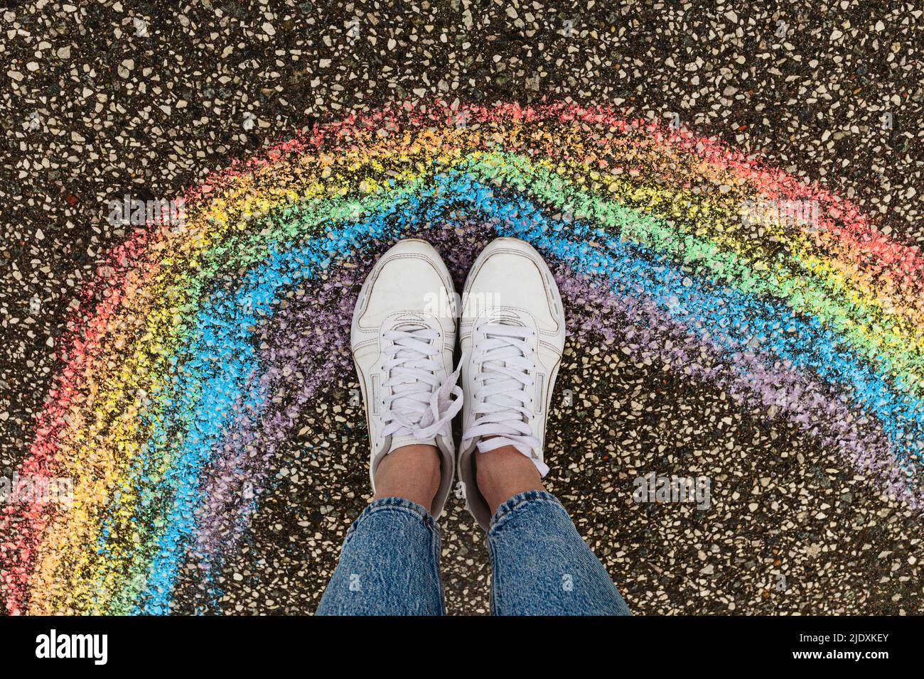 Frau in weißen Schuhen, die auf der Straße neben einer Regenbogenzeichnung steht Stockfoto