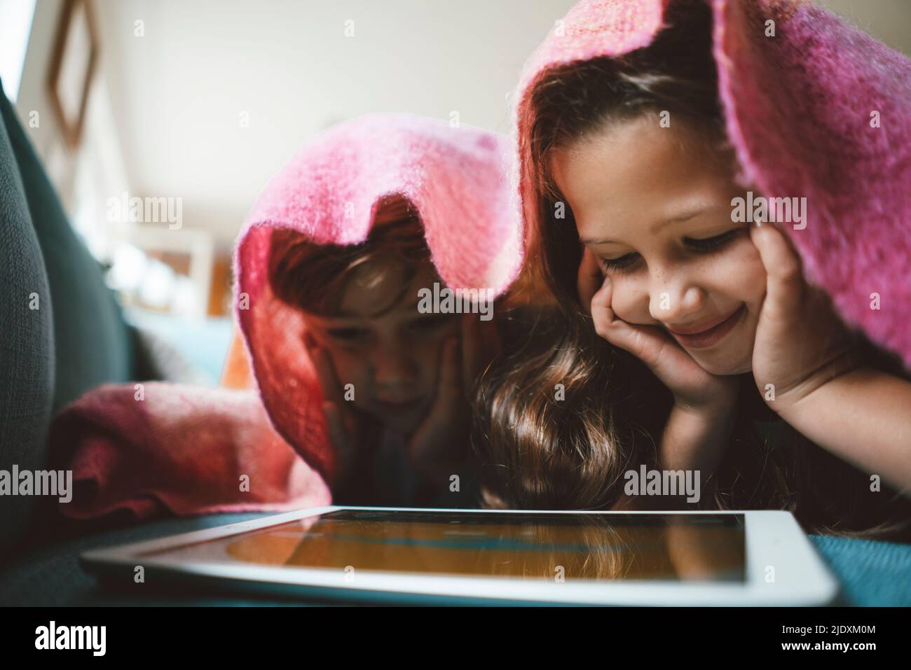 Glückliche Geschwister mit Kopf in den Händen, die einen Tablet-PC zu Hause unter der Decke liegen lassen Stockfoto