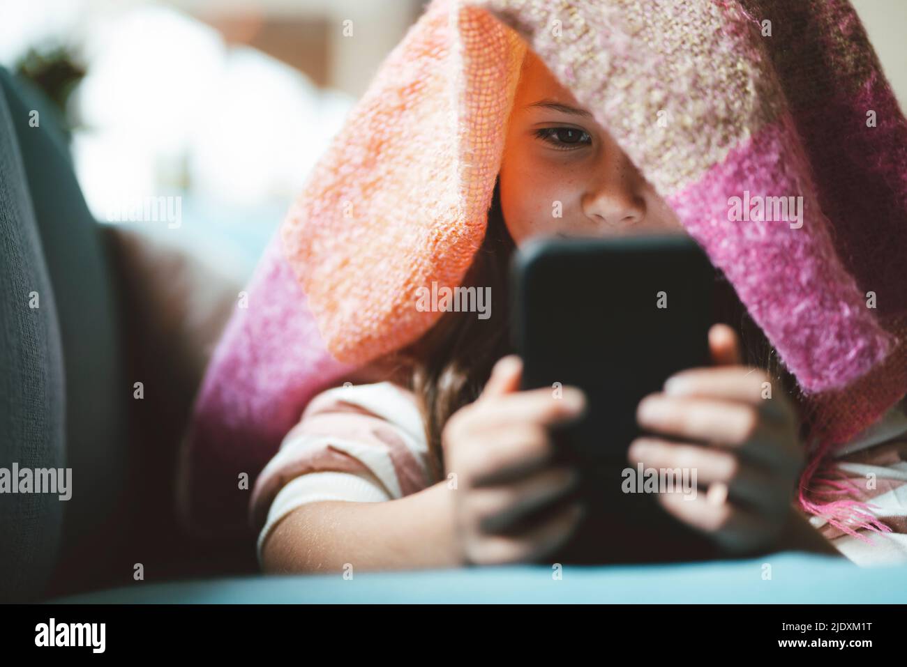 Mädchen mit Smartphone unter der Decke zu Hause liegen Stockfoto